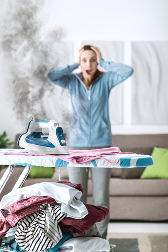 Shocked woman gasping at home, she has left the iron on and she is burning her clothes
